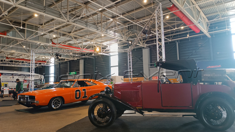 une strutcure aluminium en forme de L garnie de projecteurs placée derriere deux voitures de collection délimite le stand de rétromobile