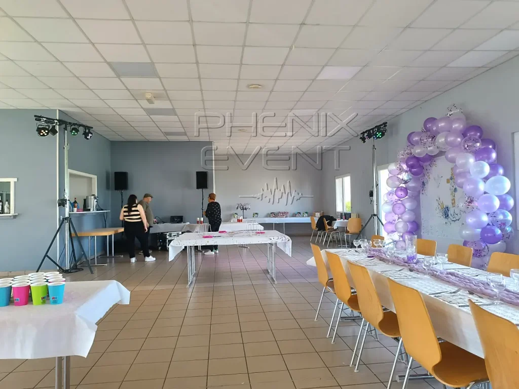 Installation du système de sonorisation 1200w et pack projecteurs pour une communion à la salle des fêtes de Flétrange, avec une arche de ballons mauves à droite, des tables et des chaises.
