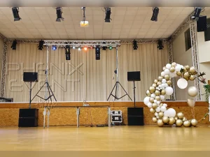 une sono 3000 watts stack et un pont en aluminium avec des jeux de lumières sont installés au centre d'une scène, à côté d'une arche de ballons