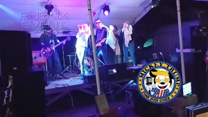 Mickey Trump sur scène interprète Still Loving You. La chanteuse, micro en main et bras levé, est entourée des autres membres du groupe et d'un chœur spécialement formé pour l'occasion.