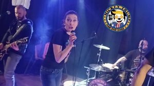 Mickey Trump interprétant "Take On Me" en live sur la scène de la mairie de Fillières. Marine, la chanteuse du groupe, tient en main un micro et semble très contente d'interpréter cette chanson