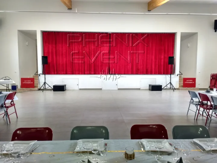 Sono 2000W Phenix Event louée et installée devant la scène, munie de rideaux rouges, de la salle des fêtes de Solgne.
