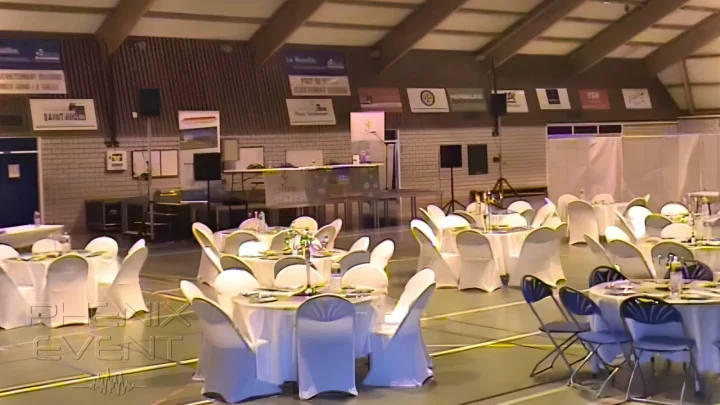 Vue générale du gymnase de la Carrière avec tables décorées au premier plan, scène et système de sonorisation 2000w en arrière plan